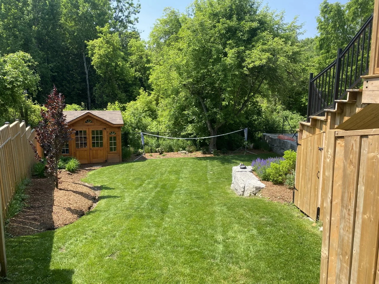 A backyard garden with planted beds, a lawn and a wood shed